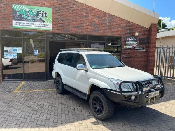 White Toyota Land Cruiser Prado 120 Series parked outside the AutoFit workshop showing a custom steel replacement front bumper with recovery winch and integrated LED light bars