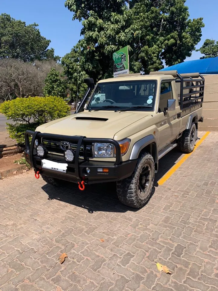 Sand-colored Toyota Land Cruiser 79 single-cab parked outside showing heavy-duty replacement bumper, LED spotlights, snorkel, and custom black cattle cage