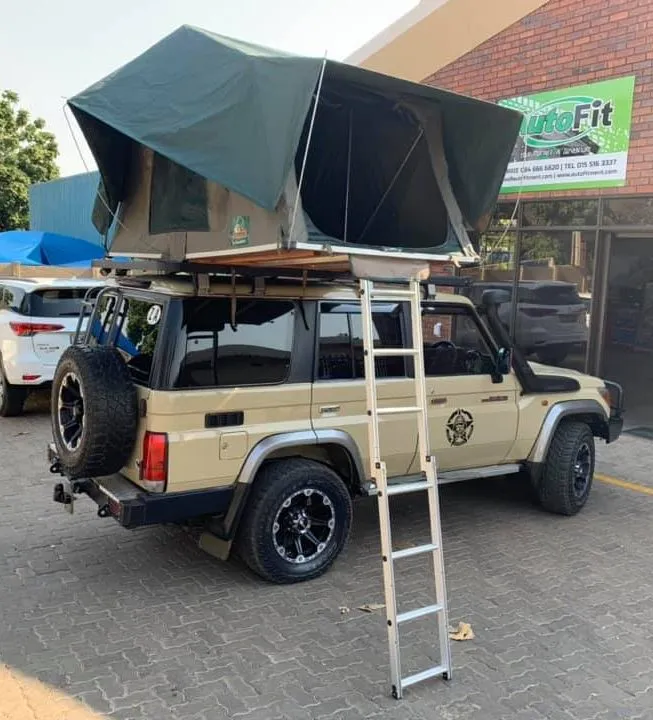 Beige Toyota Land Cruiser 76 station wagon parked outside the AutoFit workshop with an open soft-shell rooftop tent and ladder set up