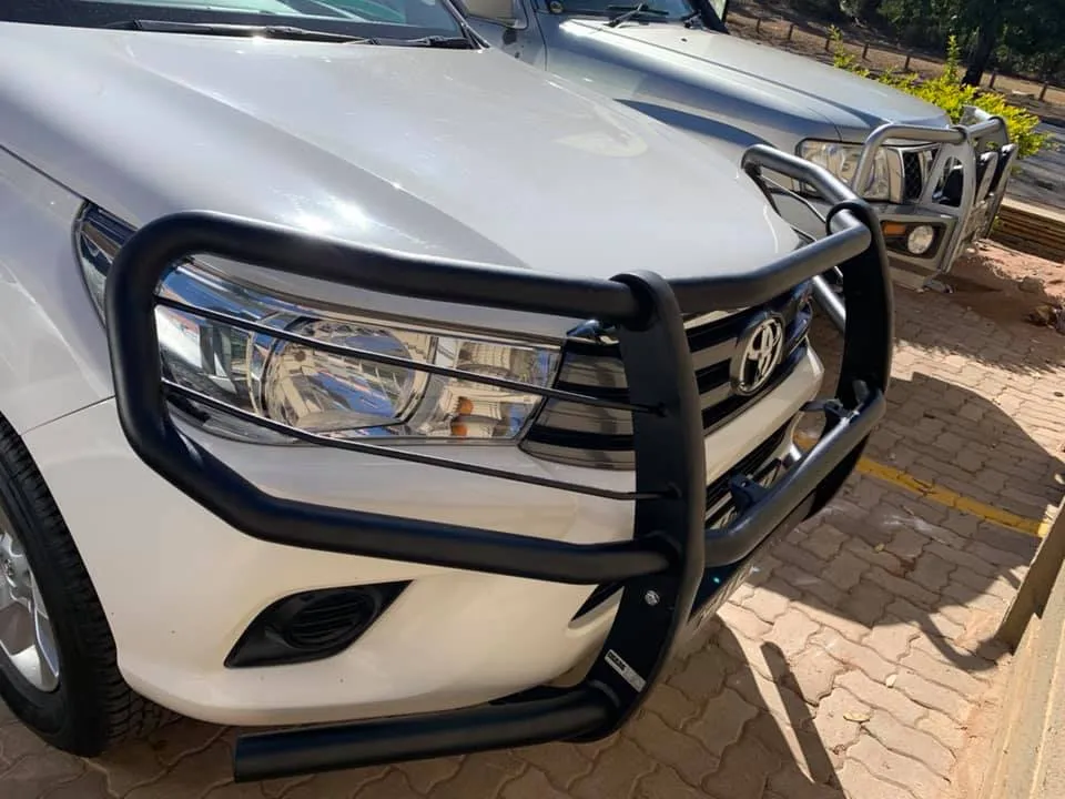 Front view of a white Toyota Hilux equipped with a matte black wrap-around steel bull bar protecting the headlights and grille
