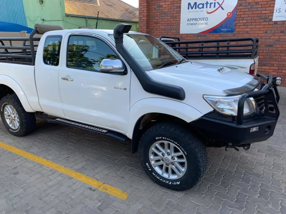 Toyota Hilux Extra Cab fitted with a black steel replacement front bumper (bull bar), Safari snorkel, side steps/rock sliders, and load bin cattle rack.