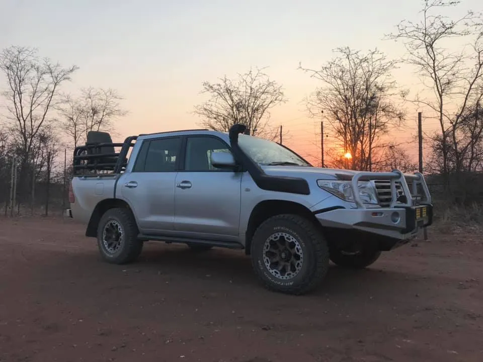 Silver Toyota Land Cruiser 200 double-cab pickup conversion showing a color-coded front replacement bumper, snorkel, and rear hunting frame with high-level seat