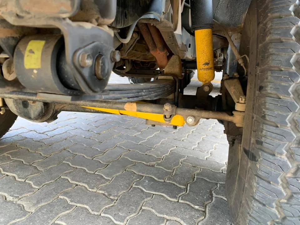 Undercarriage view of a 4x4 vehicle showing a yellow Old Man Emu steering damper and matching OME shock absorber with leaf springs