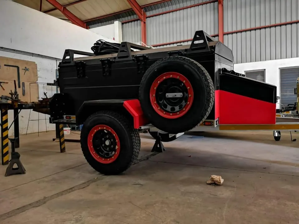 Heavy-duty off-road camping trailer customized with red and black accents, red beadlock-style wheels, and custom-built chassis.