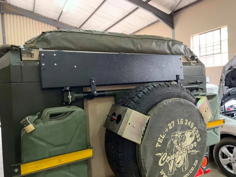 Conqueror Off-Road trailer rear setup featuring dual 20L plastic jerry cans mounted in steel holders, spare wheel with Conqueror cover, and a top mounting rack.