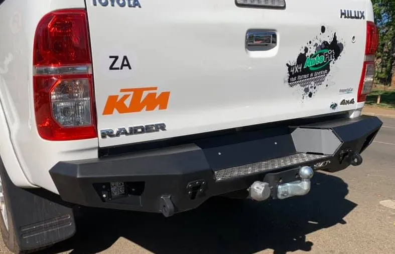 Rear view of a white Toyota Hilux Raider showing a heavy-duty matte black steel replacement bumper with integrated tow bar and step