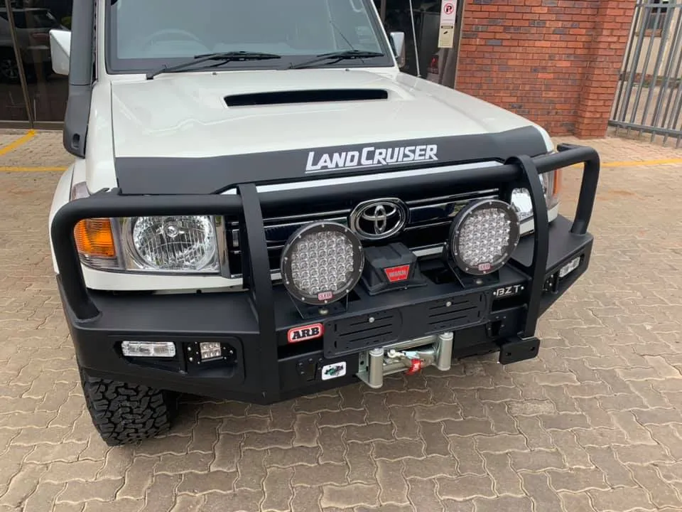 White Toyota Land Cruiser 70 series front view showing a black steel bumper, integrated Warn winch, and round LED spotlights