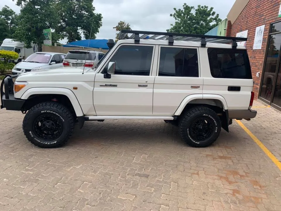Left side profile of a white Toyota Land Cruiser 76 station wagon fitted with a roof rack, snorkel, and black wheels